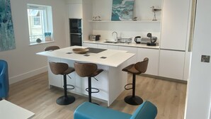 A modern kitchen with a central island, bar stools, and a dining table. - Stunning Cliff Edge Apartment in Newquay (Newquay)