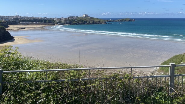 A coastal view with a beach, a rocky outcrop, and a building on a hill. - Stunning Cliff Edge Apartment in Newquay (Newquay)
