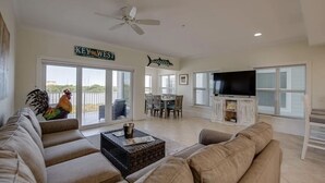A spacious living room with a large TV, comfortable seating, a ceiling fan, and a view of the outdoors.