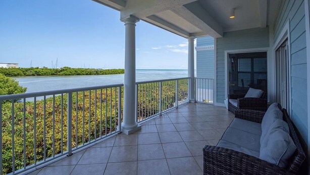 A covered porch with a view of the ocean, a wicker sofa, and a railing.