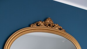 Un espejo con un marco dorado ornamentado sobre una pared azul.