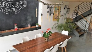 Een eetgedeelte met een houten tafel, witte stoelen, een schoolbord met een citaat en een trap.