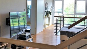 Een ruime woonkamer met een houten vloer, een televisie, een plant en een trap naar een hoger niveau.