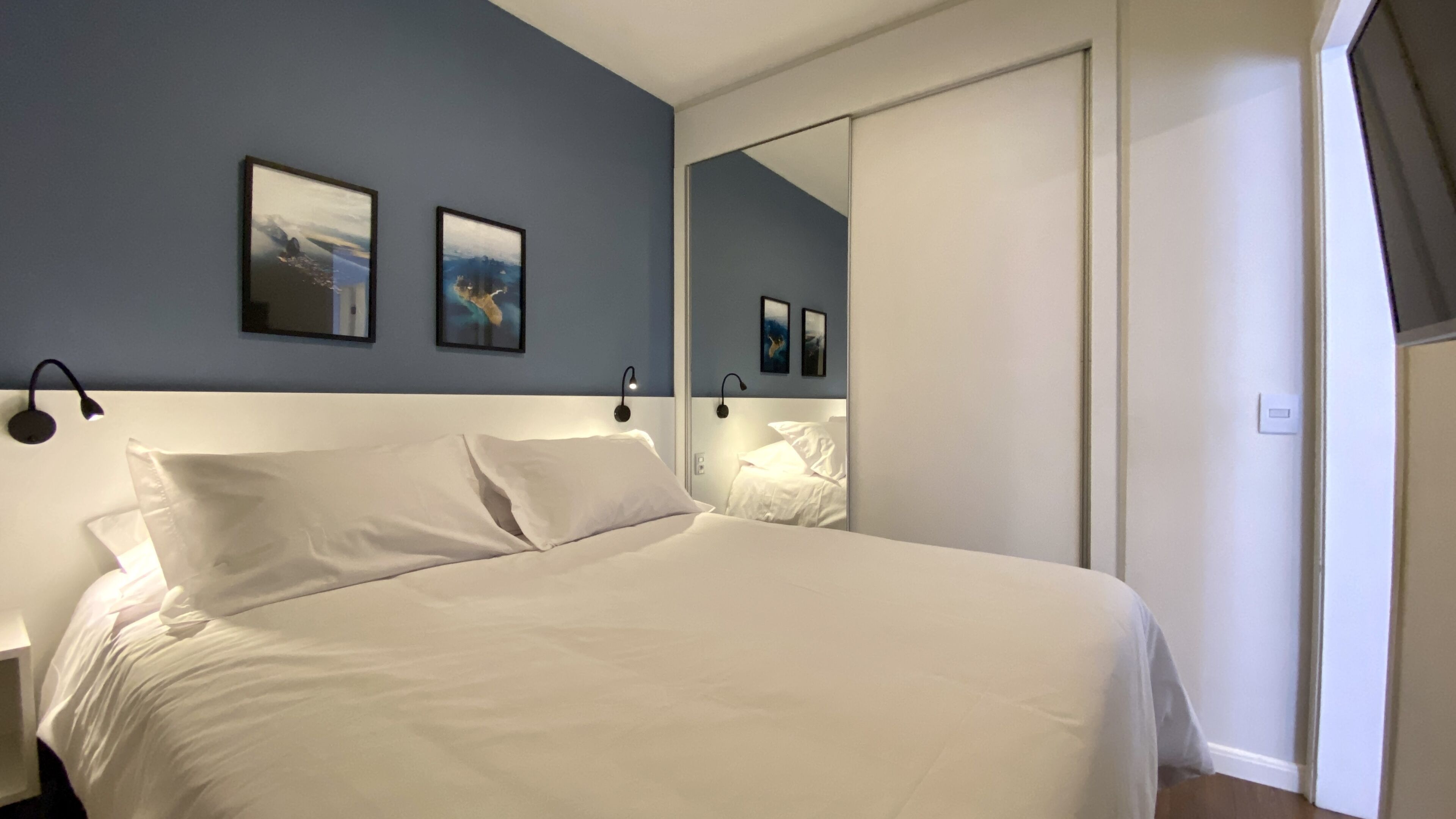 Une chambre à coucher avec un lit, deux lampes fixées au mur et deux tableaux encadrés accrochés au mur.