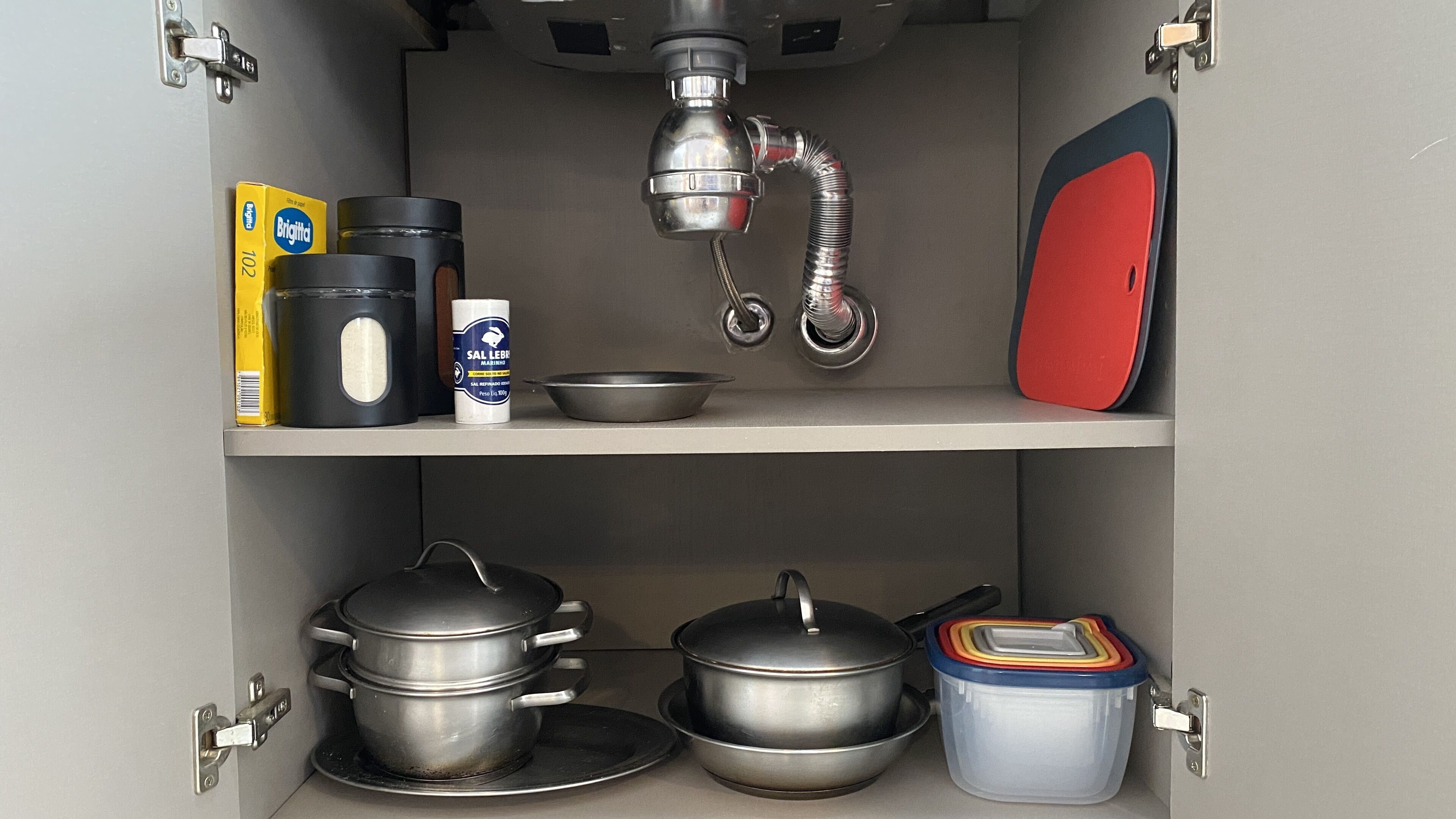 A kitchen cabinet with pots, pans, a frying pan, a saucepan, a container, and a box of salt.