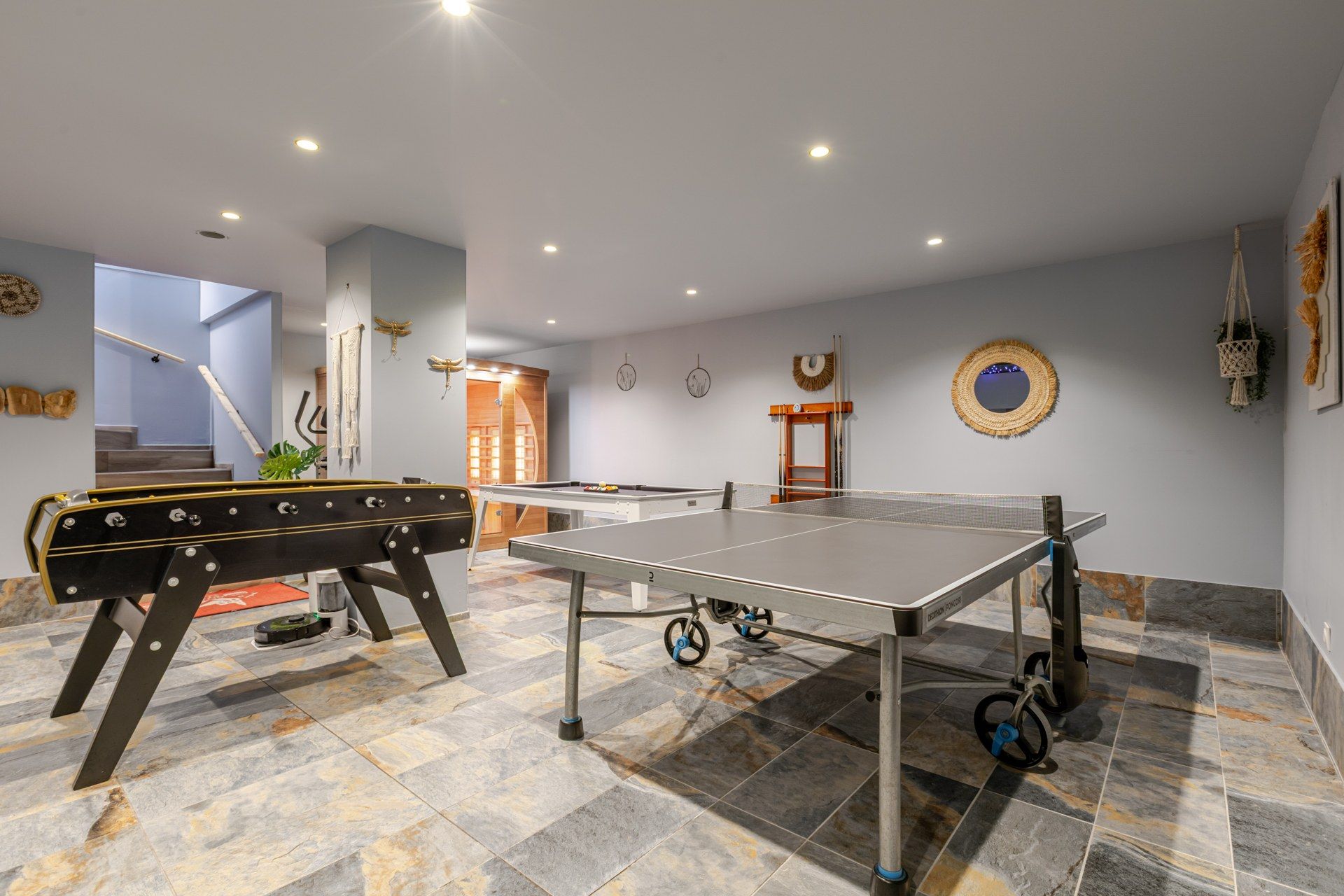 Une pièce équipée d’une table de ping-pong, d’un baby-foot et d’un escalier menant à un autre niveau.