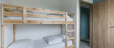 A bunk bed with white bedding, a wooden ladder, and a wardrobe in the adjacent room.