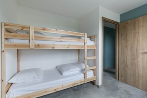A bunk bed with white bedding, a wooden ladder, and a wardrobe in the adjacent room.
