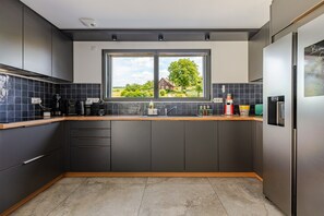 Una cocina moderna con armarios oscuros, encimera de madera y ventana con vistas a una casa y vegetación.