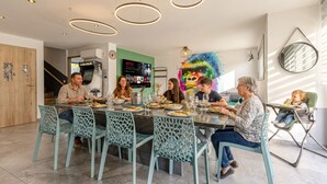 Ein Essbereich im modernen Stil, mit einem zentralen Tisch, Stühlen, einem an der Wand befestigten Fernseher und einem farbenfrohen Kunstwerk.