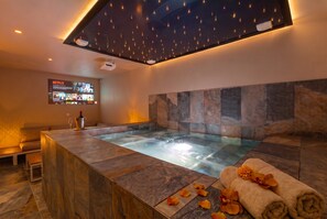Ein moderner Wellnessraum mit Whirlpool, einer Sitzecke und einem an der Wand montierten Bildschirm, der eine Netflix-Oberfläche zeigt.