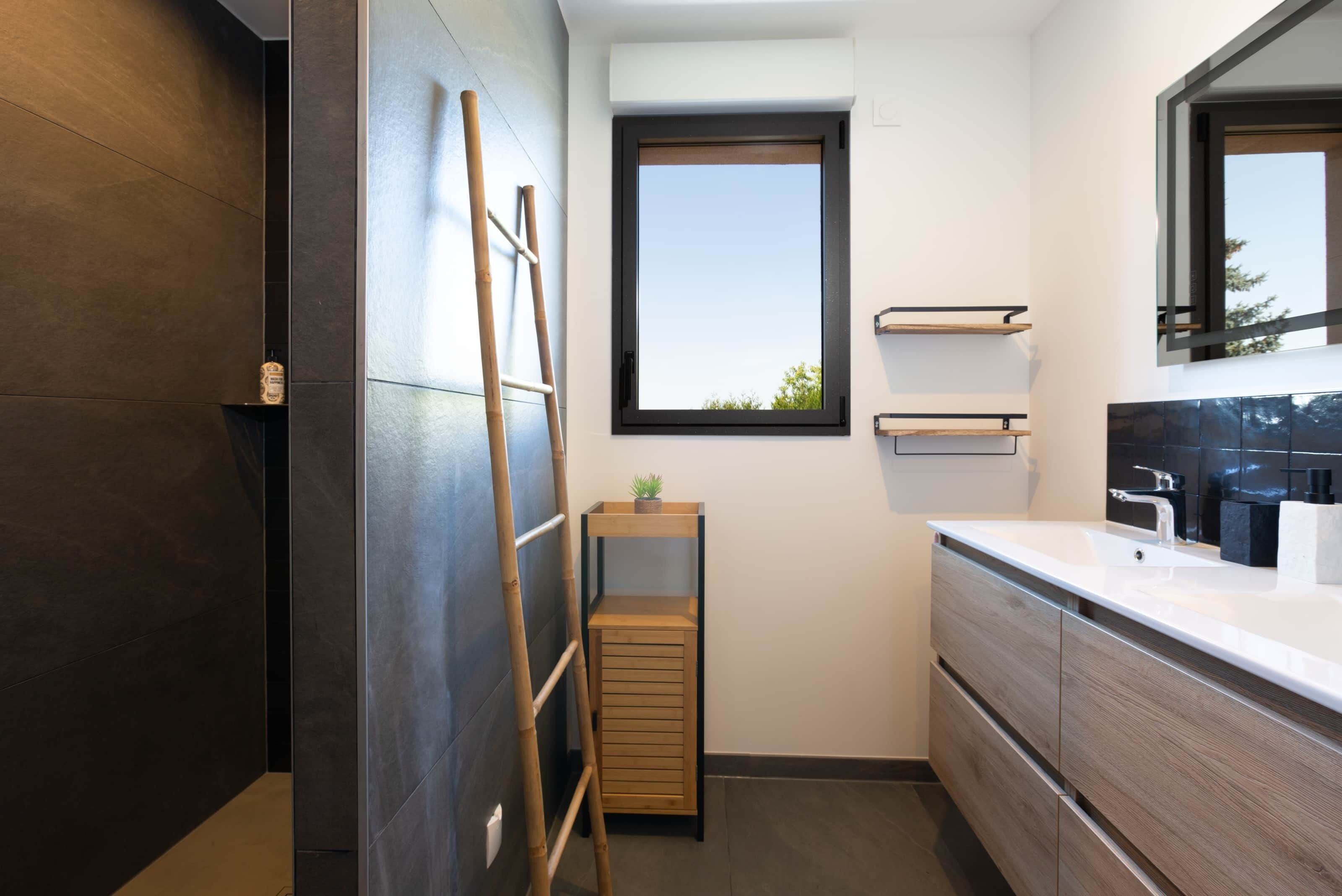 A modern bathroom with dark wooden walls, a large window, and a wooden ladder.