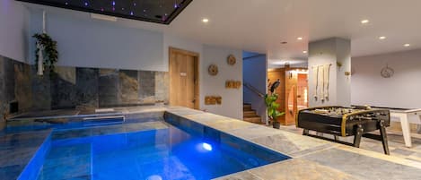 A modern indoor pool area with a clear blue pool, stone flooring, and a ceiling with star projections.