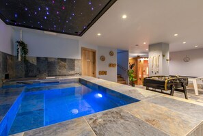 A modern indoor pool area with a clear blue pool, stone flooring, and a ceiling with star projections.