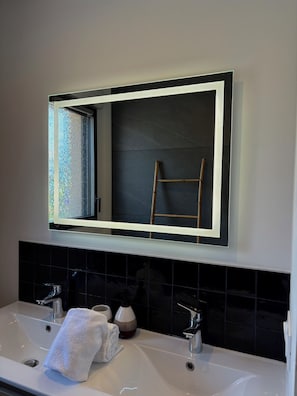 A bathroom with a large mirror, two sinks, and a towel rack.