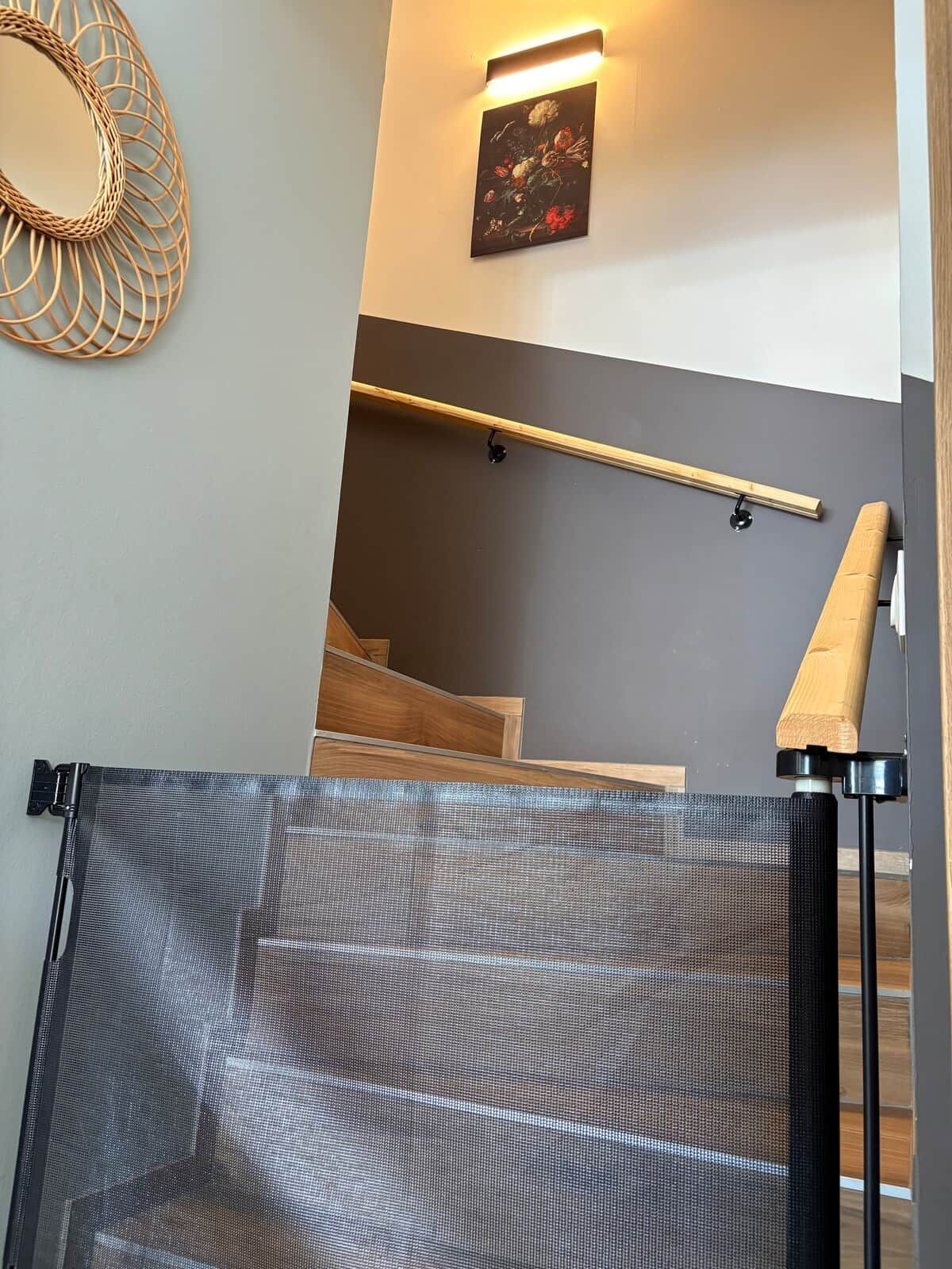Une pièce avec un escalier en bois, un tableau accroché au mur et un portail en métal.