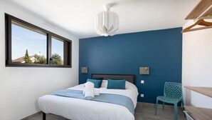 Un dormitorio con cama, ventana, silla y ventilador de techo.