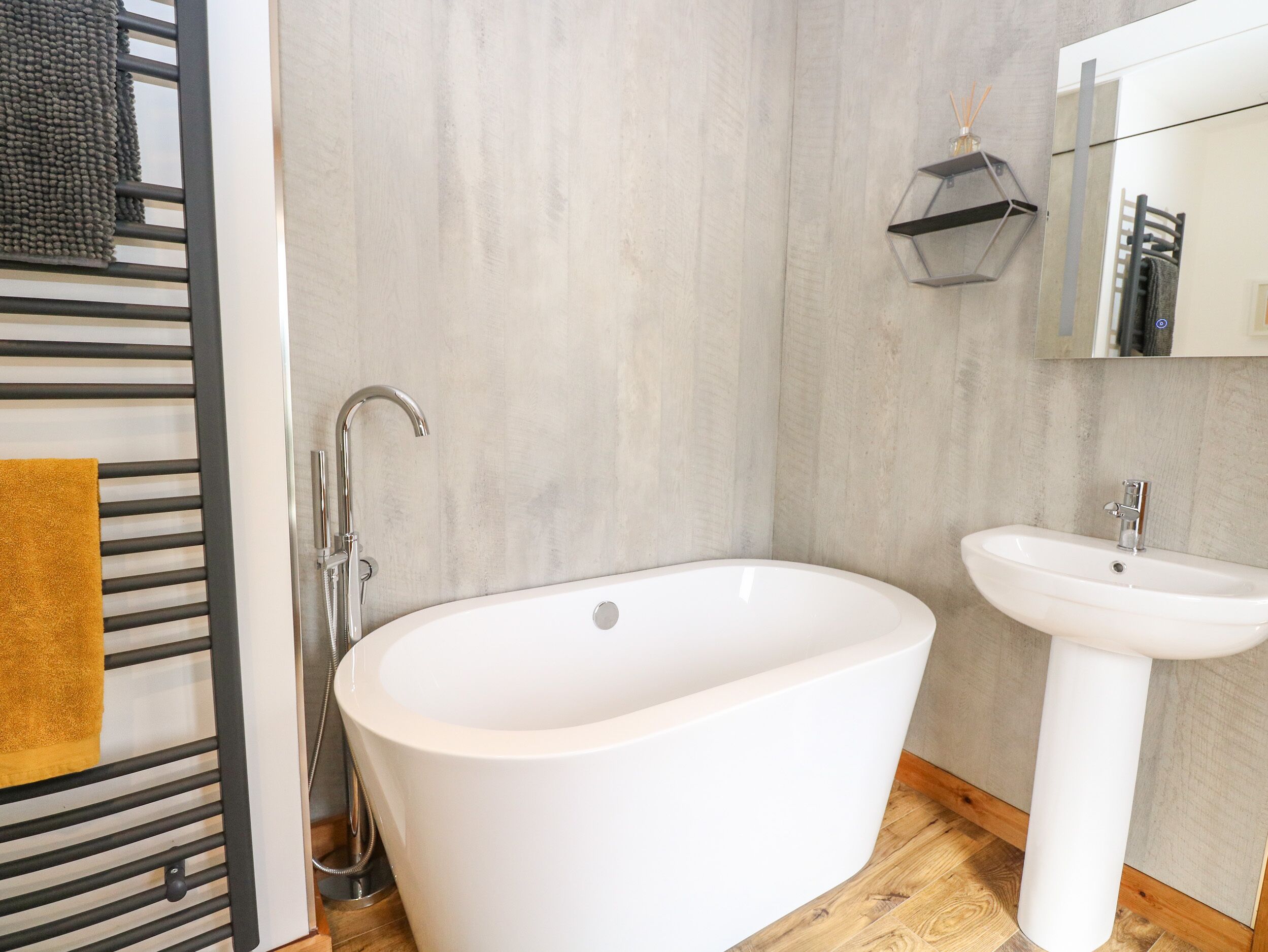 Ein modernes Badezimmer mit einer freistehenden Badewanne, einem weißen Waschbecken und einem Handtuchhalter mit einem gelben Handtuch.