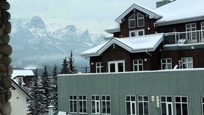 Un immeuble à plusieurs étages, dont le toit est recouvert de neige, avec de grandes fenêtres et une vue sur des montagnes enneigées en arrière-plan.