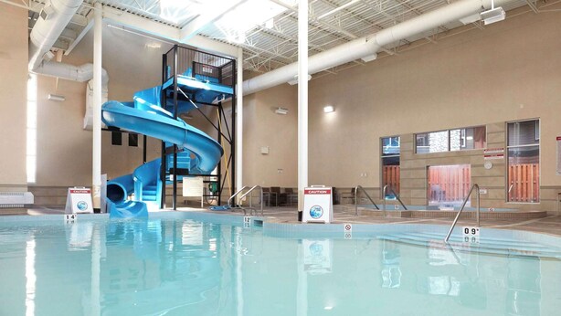 Une piscine intérieure avec un toboggan bleu et un panneau d’avertissement.