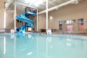 Una piscina interior con un tobogán de agua azul y un letrero de precaución.