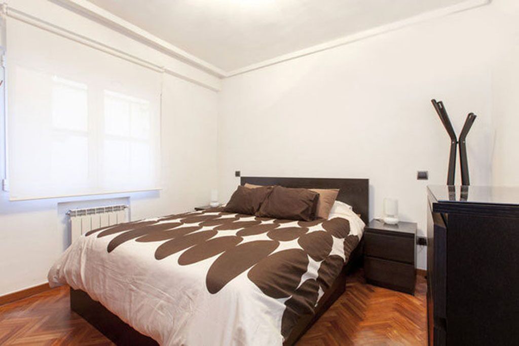 Un dormitorio con cama, mesita de noche, cómoda y radiador.