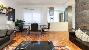 A modern living room with a sofa, a coffee table, and a dining area with chairs and a table. There is a kitchen area visible in the background. - Luxury Flat in Madrid center (Madrid)