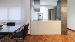 A modern kitchen with white cabinets, a stainless steel refrigerator, and a microwave. There is a dining area with a glass table and black chairs. - Luxury Flat in Madrid center (Madrid)