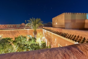 A courtyard with a palm tree, a large wall with battlements, and a dome structure in the background.
