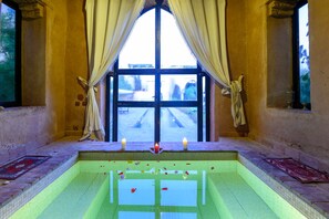 A room with a large window, a pool with floating candles, and a view of a courtyard.