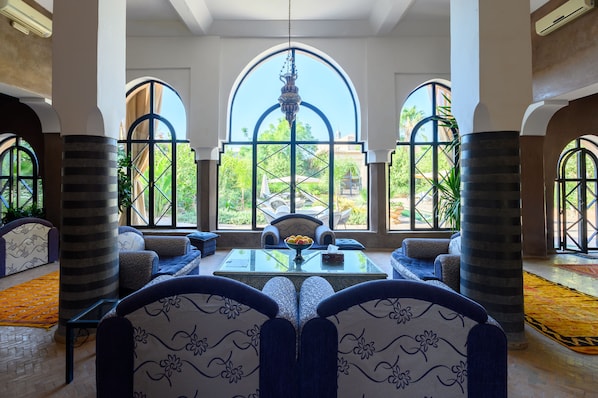 A spacious lounge area with a large arched window, comfortable seating, and a central table.