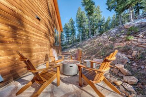 A wooden cabin with a stone patio, outdoor seating, and a fire pit.