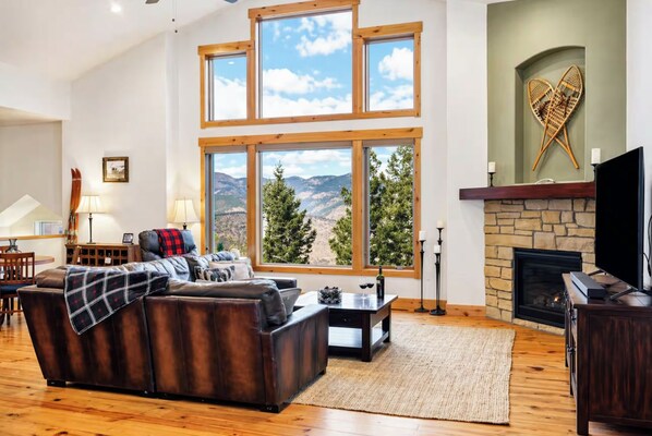 A living room with a fireplace, a large window with a mountain view, a sofa, and a television.