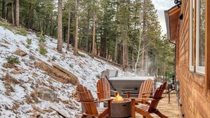 A wooden cabin with a stone patio, outdoor seating, and a fire pit.