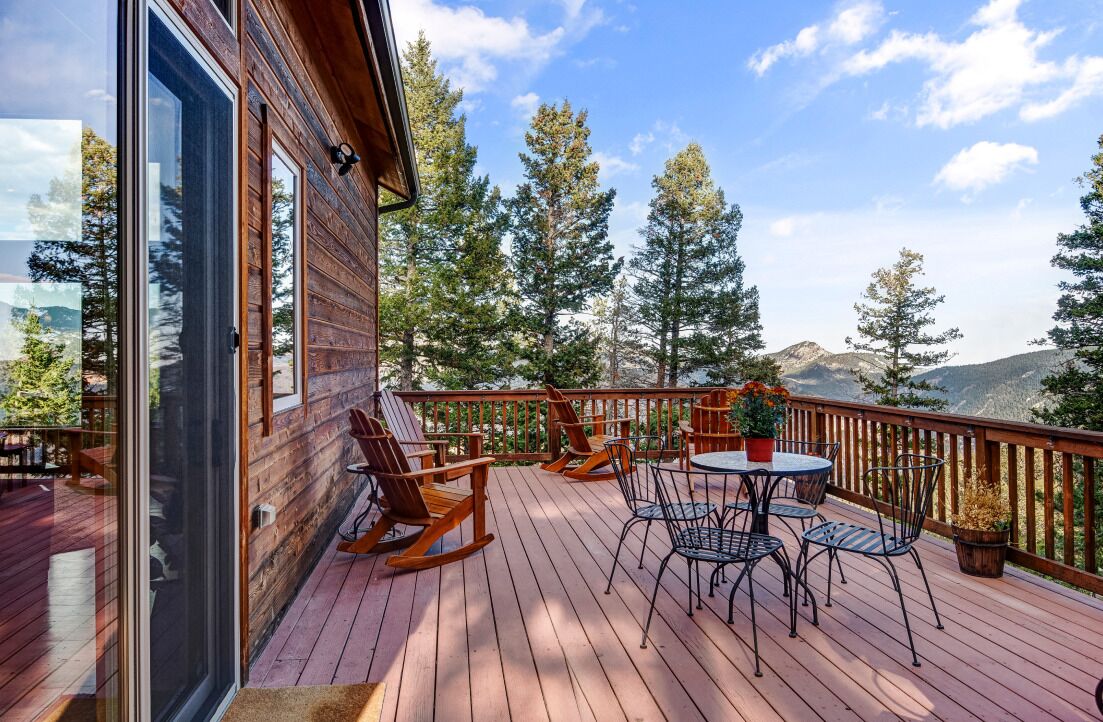 A wooden deck with outdoor furniture, including rocking chairs and a table, overlooking a mountainous landscape.