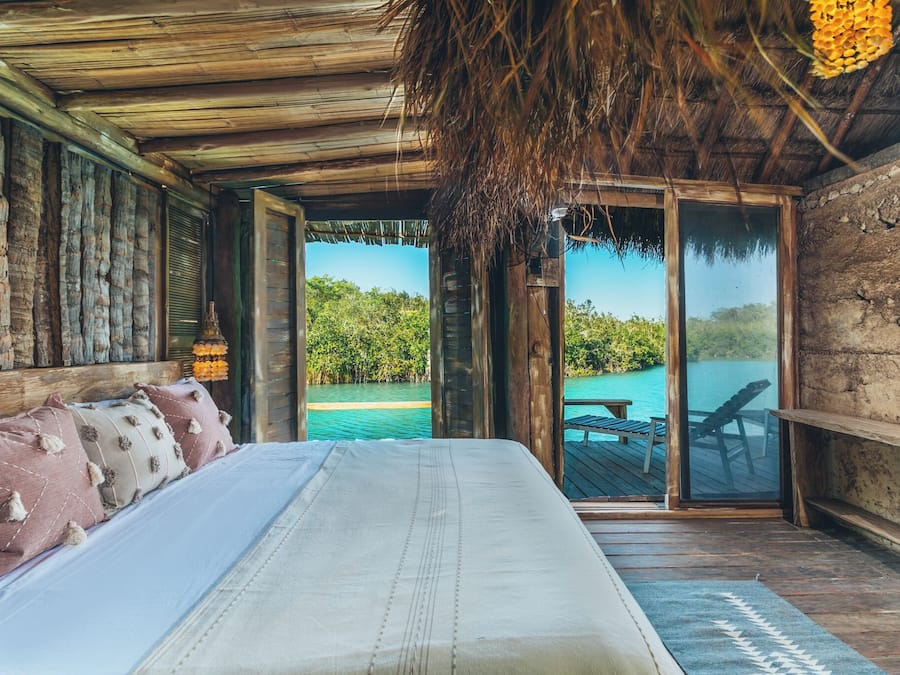 A wooden room with a bed, a hanging light fixture, and a view of a body of water.