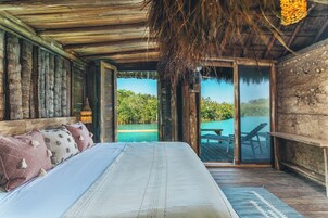 Una habitación de madera con una cama, una lámpara colgante y vista a un cuerpo de agua.