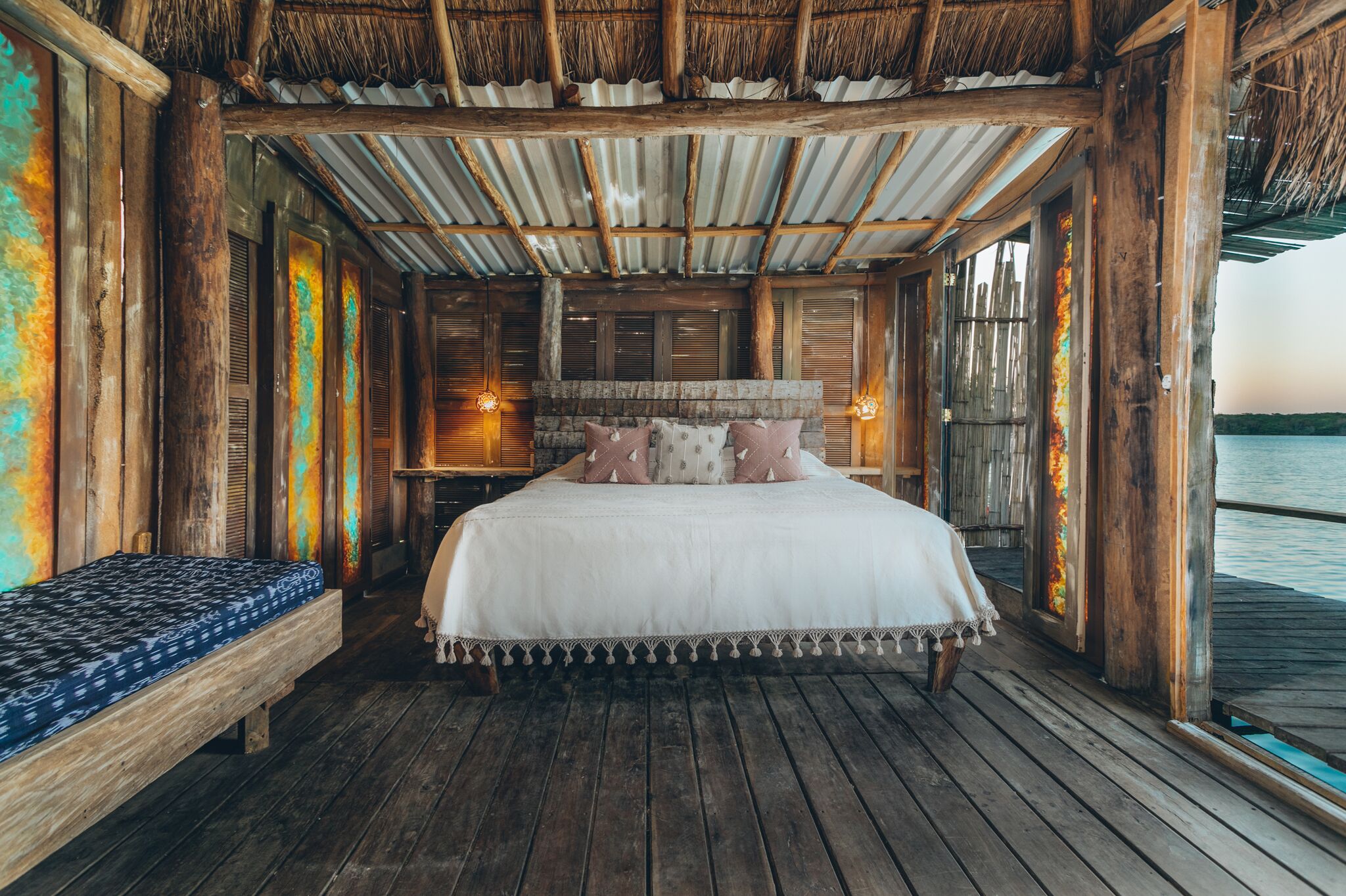 A wooden room with a bed, a bench, and a view of the water.