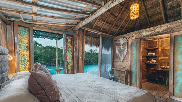 Een slaapkamer met een bed, uitzicht op de oceaan en een rieten dak.