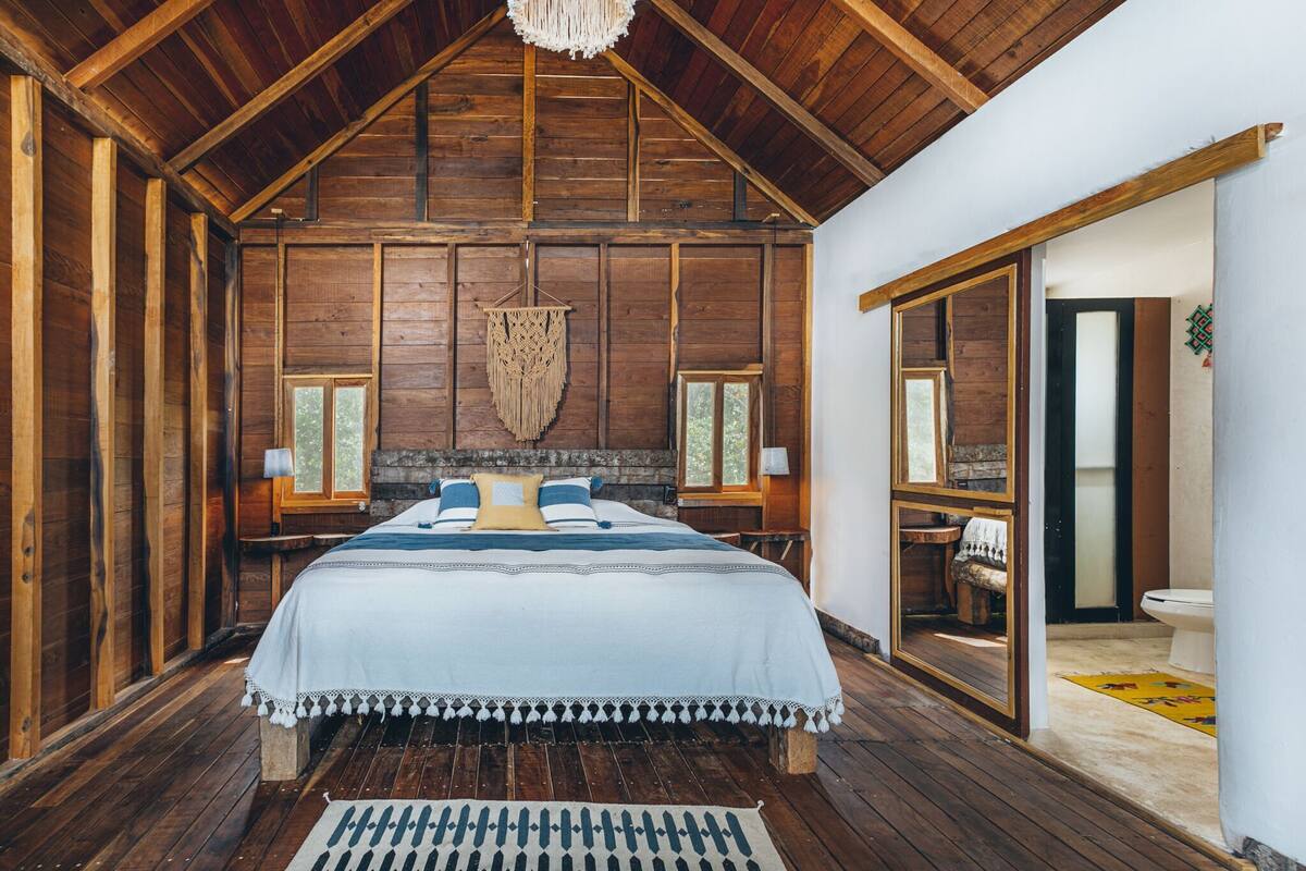 Ein Schlafzimmer mit Holzboden und -wänden, ein großes Bett und Blick ins Badezimmer.