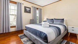 Une chambre à coucher avec un grand lit, une table de chevet, une fenêtre avec des rideaux et un radiateur.