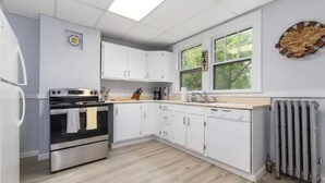 Une cuisine moderne avec des meubles blancs, un four en acier inoxydable, une machine à café et une fenêtre donnant sur un paysage verdoyant.