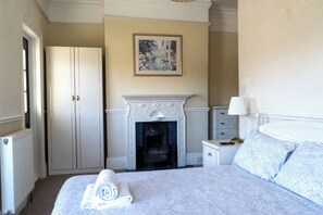 Habitación de hotel con cama, chimenea, armario y mesita de noche con lámpara.