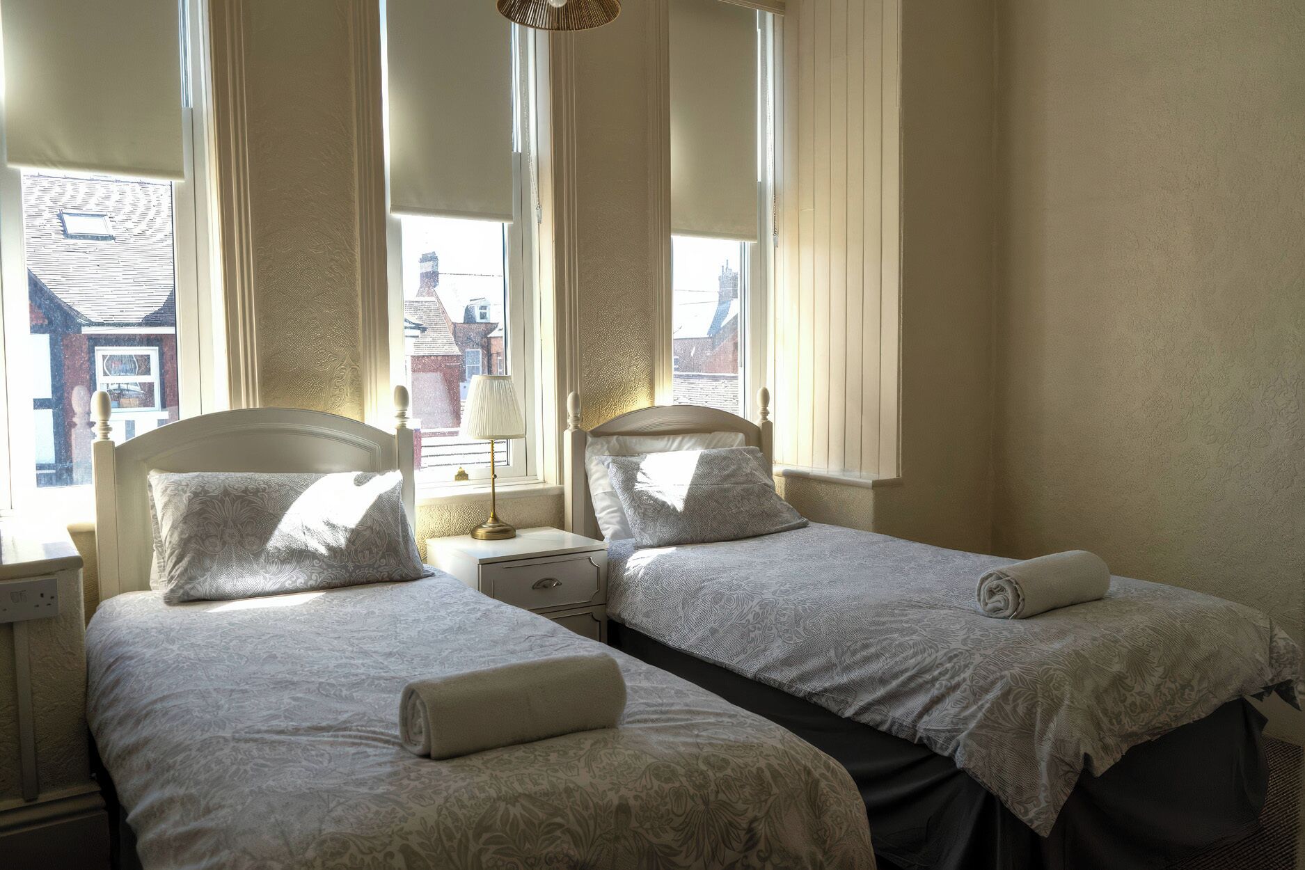 A twin room with two beds, a nightstand, a lamp, and a window with a view of buildings.