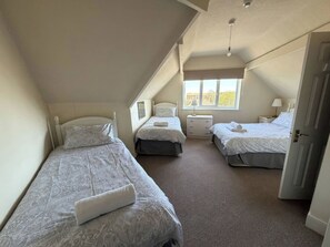 Quarto sótão triangular com três camas, uma janela e uma porta.