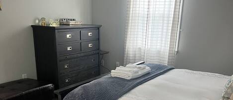 A bedroom with a bed, a dresser, a window with curtains, and a patterned rug.
