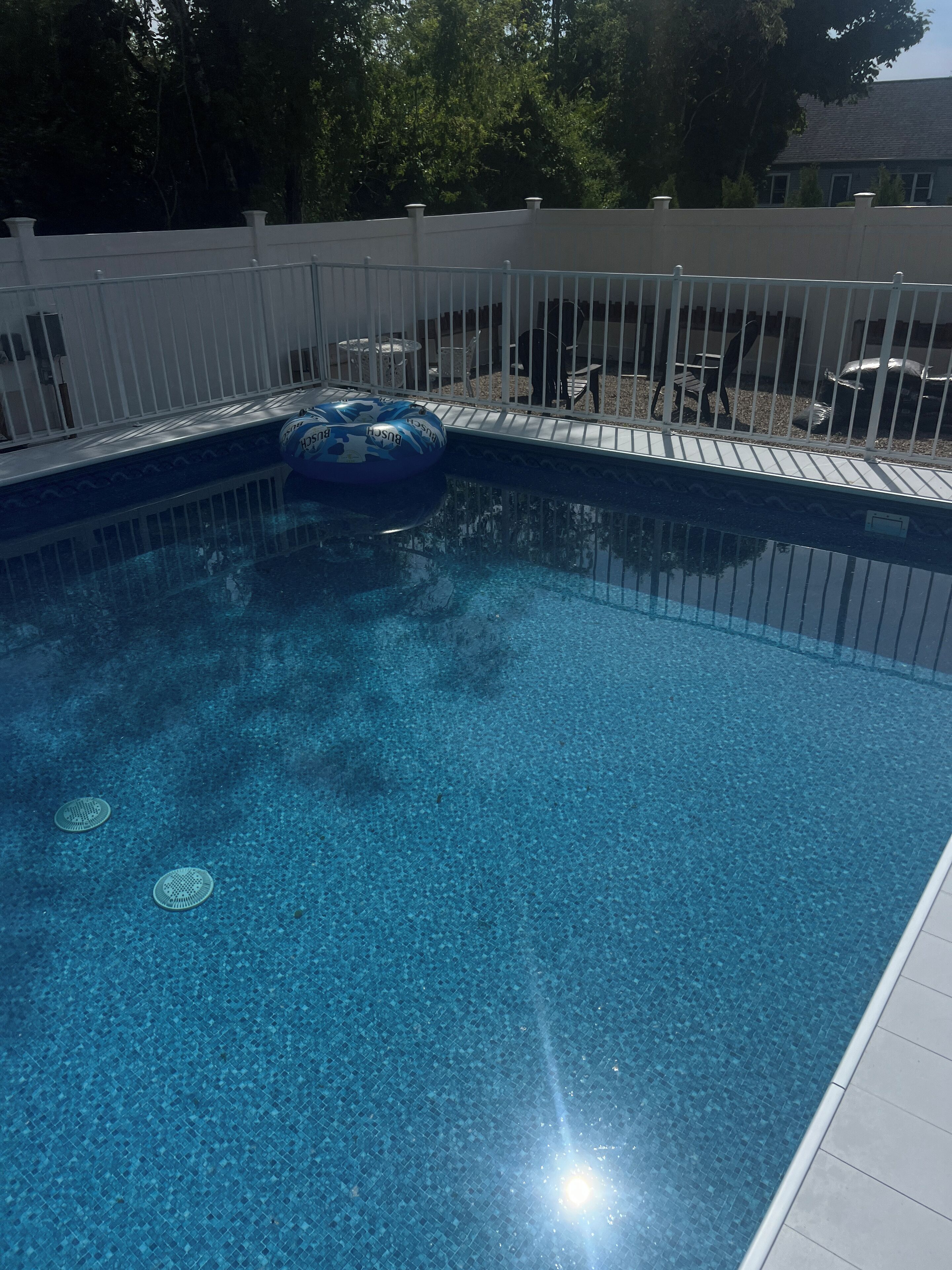 Ein Swimmingpool mit weißem Zaun, einem blauen Schwimmreifen und einer gefliesten Terrasse.