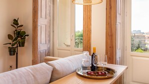 Une pièce chaleureuse avec une table en bois sur laquelle sont disposés une bouteille, des verres et des amuse-gueules. Une lampe en osier est suspendue au-dessus de la table, et une plante se trouve sur la gauche.