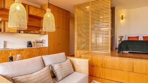 Un intérieur moderne avec un coin cuisine en bois, un canapé avec des coussins à rayures et un lit avec des oreillers rouges.