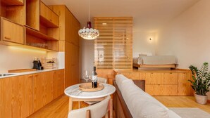 Een kleine keuken met houten kastjes, een eethoek met een ronde tafel, en een zithoek met een bank.